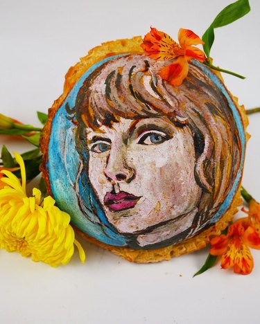 Sourdough loaf painted with the face of a woman with dark blonde hair and bangs