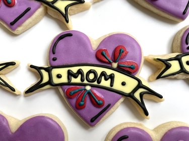 Purple heart-shaped Mother's Day cookie with word "mom" on banner and decorated with red flowers