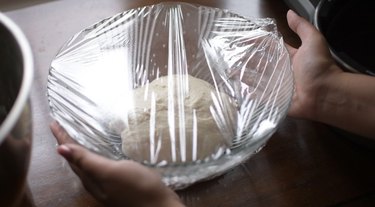 Dough resting in bowl covered with plastic wrap