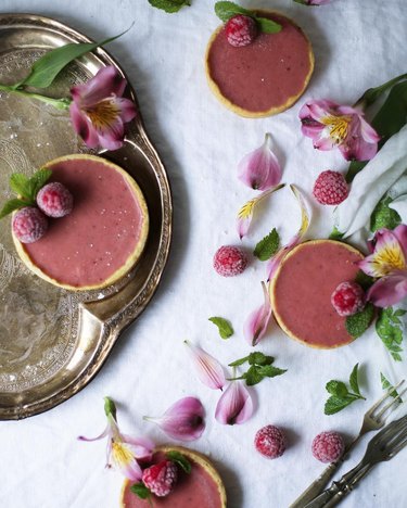 Circular pink tarts with raspberries and flower petals strewn on top