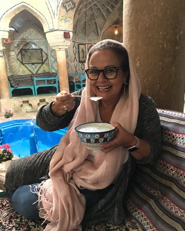 Woman with glasses and light pink headscarf eating with a spoon from a bowl