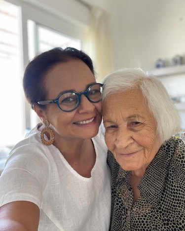 Two women, one in glasses and dangly earrings and the other with white hair, smile side by side