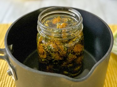 jar of dried dandelion flowers and coconut oil placed in a saucepan with water