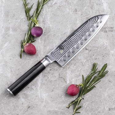 Shun santoku with black handle, pictured on a grey marble counter with vegetables