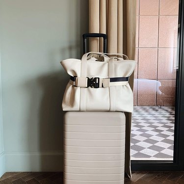 Cincha belt in black and white attaching a large tote bag to the telescoping handle of a suitcase.