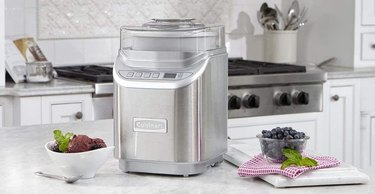Cuisinart ice cream maker on marble counter in high-end kitchen, with fresh berries and finished ice cream