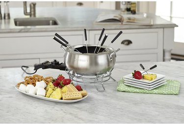 Cuisinart electric fondue maker set up for chocolate fondue, with fruit, marshmallows and baked goods for dipping, in a high-end kitchen