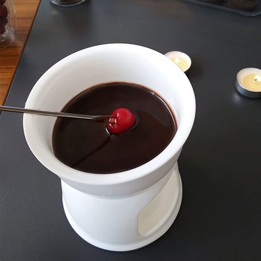 White ceramic mini-fondue pot shown on a black countertop, with a tea light in the background