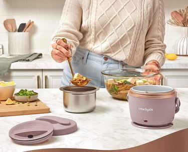Woman in sweater dishing food into pale pink Crockpot Electric Lunch Box.