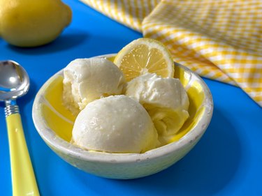 Lemon ice cream scoops in a bowl with a wedge of lemon