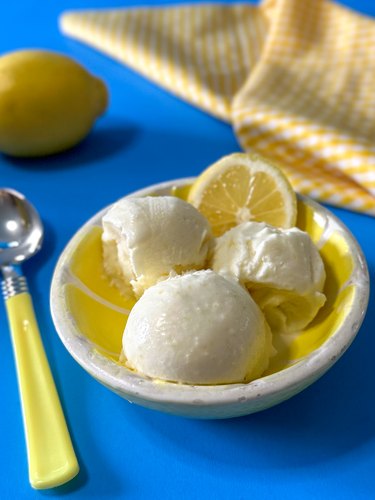 three lemon ice cream scoops in a bowl with a lemon wedge