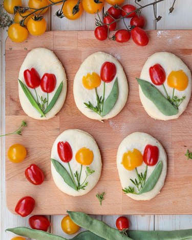 Small loaves of dough with tulips formed from cherry tomatoes and greenery