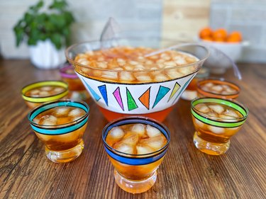 Colorful painted punch bowl surrounded by several matching glasses filled with orange icy liquid
