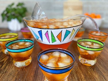 Colorful painted punch bowl surrounded by several matching glasses and filled with orange icy liquid