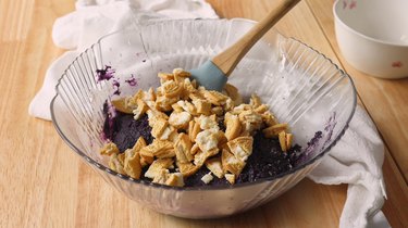 Ube cookie dough batter in a glass mixing bowl with chopped golden Oreos on top, ready to be mixed.