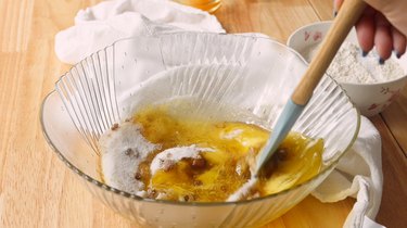 Mixing melted butter and sugars in a glass mixing bowl.