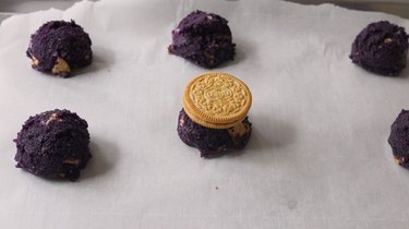 Ube cookie dough balls on lined baking tray; one has an entire Golden Oreo on top.