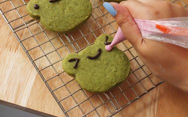 Using a piping bag to add pink blush to frog shortbread cookie