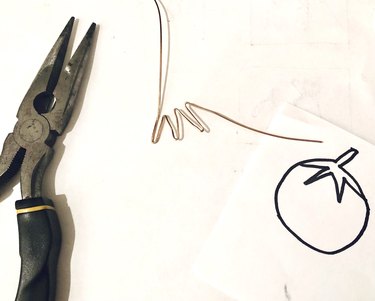 An image of folded wire, pliers, and a drawing of a tomato