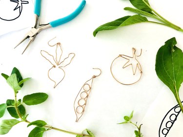 An image of wire veggie earrings surrounded by leaves and tools