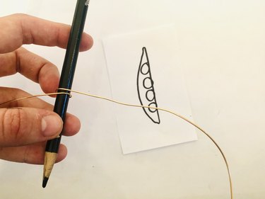 An image of wire wrapped around a colored pencil; there is a drawing of a pea pod in the background