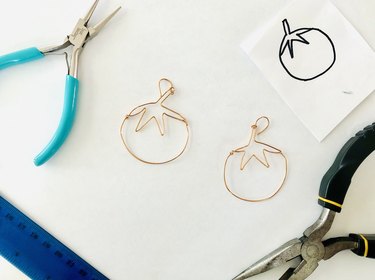An image of finished tomato earrings with ruler, pliers, and tomato drawing