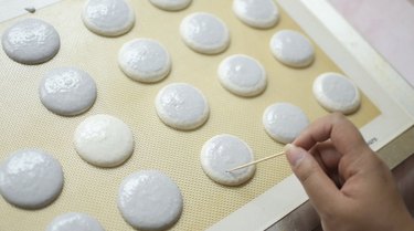 Using a toothpick to pop air bubbles on macaron shells.