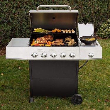 gas grill in backyard with meat and vegetables on it