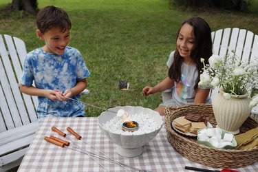 Two kids roasting marshmallows over a tabletop fire pit