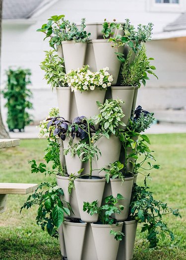 Vertical planter outdoors with various plants like flowers, tomatoes, and herbs.