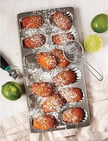 12-cup Madeleine pan with baked Madelines, lime zest, and powdered sugar on them. 