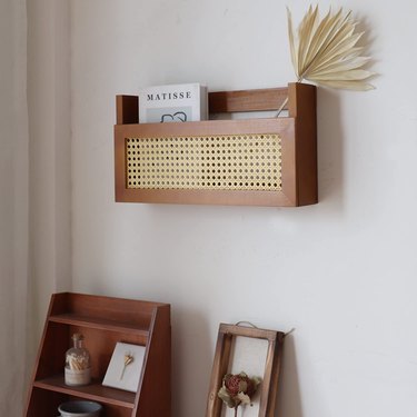 Rattan and wood wall-mounted magazine rack with a book and palm frond in it.