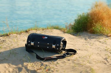 GoBQ portable grill, packed up for carrying, pictured on a patch of sand near the edge of the water