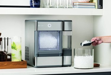 Person using GE Profile Opal Countertop Nugget Ice Maker on a countertop to scoop ice.