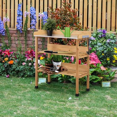 Topeakmart Potting Bench Table in Natural Wood Positioned in a Yard With Flowers and Tools on the Shelves
