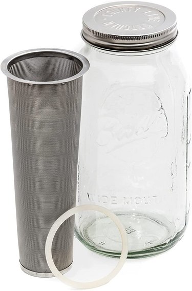 A County Line Kitchen Mason Jar Cold Brew Coffee Maker against a white background. The brewing basket is tapered and the cleaer glass mason jar has a metal twist-on lid. The photo also shows the silicone ring that seals the lid.