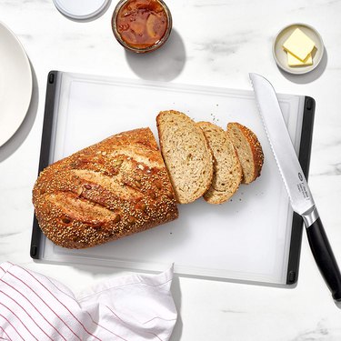 OXO plastic cutting board being used to slice a loaf of bread with a bread knife