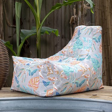 Tropical print with light gray background outdoor bean bag chair at the edge of a stock tank pool with a wood deck and fence.