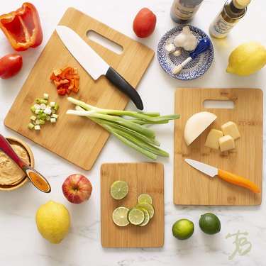 Totally Bamboo 3-Piece Bamboo Cutting Board Set on a Marble Countertop With Various Fruits and Vegetables Being Chopped