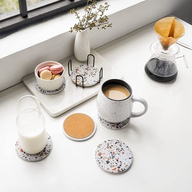 Set of 6 terrazzo coasters that fit into a metal holder displayed on a countertop with different drinks on them.