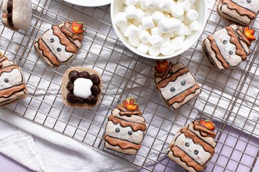 Campfire s'mores macarons on wire rack next to bowls of graham crackers and marshmallows