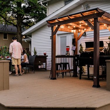 Wood and metal roof grill gazebo with string lights, a bar counter, and electrical outlets, all shielding a grill.