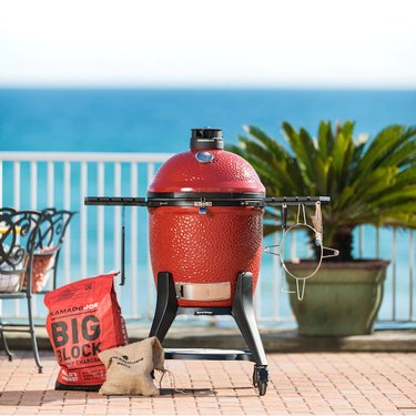 Kamado Joe Classic III grill, pictured on a patio with charcoal, and the ocean visible in the background