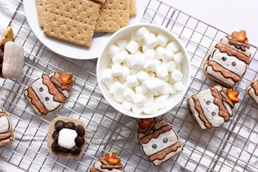 S'mores macarons on wire rack next to bowls of graham crackers and marshmallows