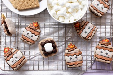 S'mores macarons on wire rack next to bowls of graham crackers and marshmallows