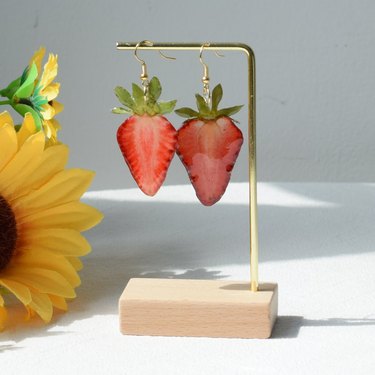 Two thin slices of real dried strawberries pressed, dipped in resin, attached to earring hooks and hanging from a gold bar