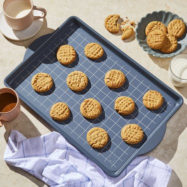 Food 52 silicone baking/pastry mat shown in a sheet pan, with cookies, displayed on a counter with coffee cups, baked cookies and a kitchen towel