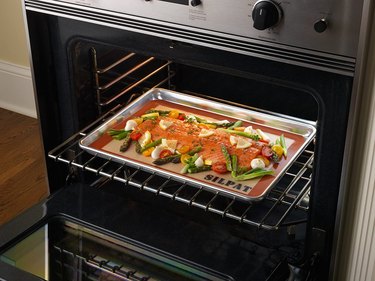 Silpat baking mat shown in an oven, with a sheet pan meal of salmon and vegetables on its nonstick surface