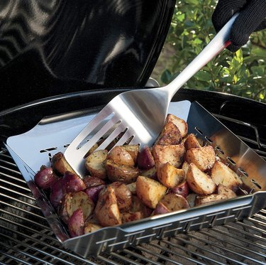 Weber grilling basket being used to roast potatoes over grill.