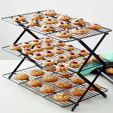 Three-tier Wilton collapsible cooling rack, depicted on a countertop filled with freshly baked cookies